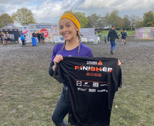 A female Spencer Clarke Group employee posing with a Tough Mudder t-shirt