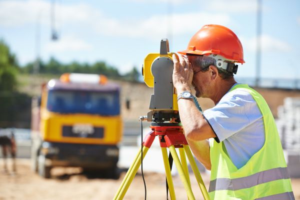 A man in high vis and an orange hard hat using a theodolite