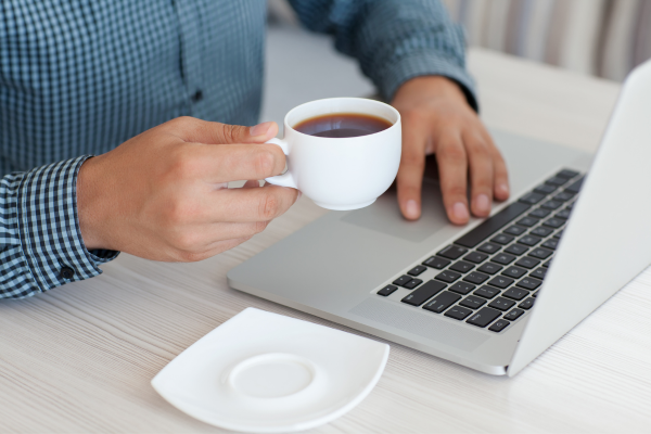 A hand holding a teacup by a laptop