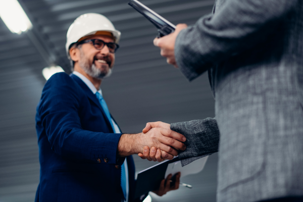 A man wearing a white hard hat and a suit shaking hands with another person
