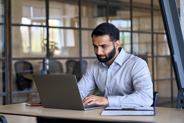 A man with a beard and wearing a grey shirt looking at a laptop