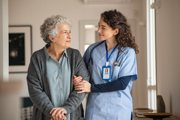 A female healthcare assistant linking arms with an elderly lady
