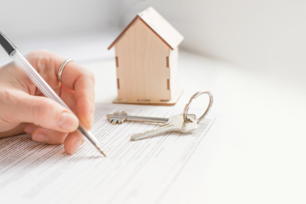A small wooden house and keys next to a hand writing on paper