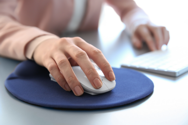 A hand holding a computer mouse that is resting on a blue mouse mat