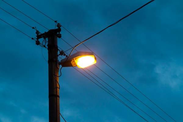 A lit street light next to telephone wires against a dark blue sky