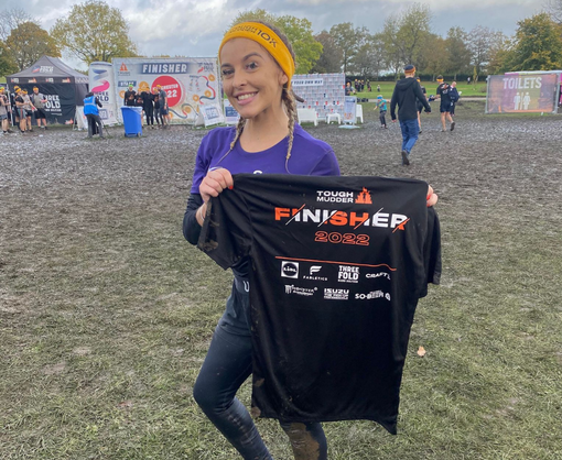 A female Spencer Clarke Group employee posing with a Tough Mudder t-shirt